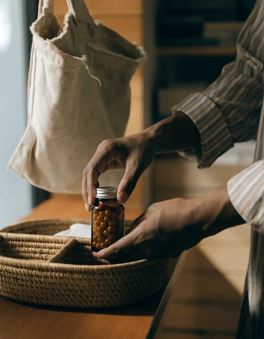 A hand resting on a wooden counter beside an unlabeled amber-glass bottle and a shallow organizer tray in morning light